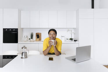 Happy freelancer sitting at the table in the kitchen with head in hands - SIF00478