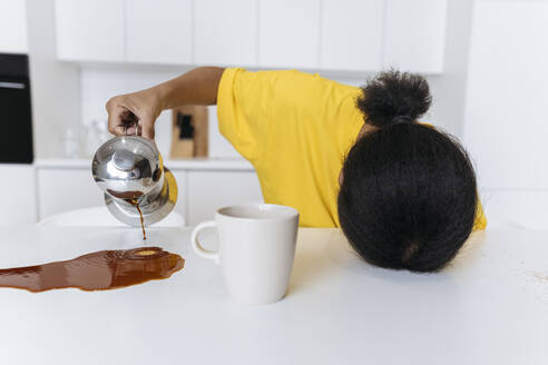Exkaustierte Frau verschüttet Kaffee auf dem Küchentisch - SIF00482