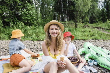 Lächelnde Frau mit Eis in der Hand sitzt mit ihren Söhnen beim Picknick - VBUF00137