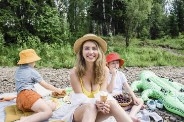 Smiling woman holding ice cream sitting with sons on picnic - VBUF00137