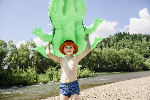 Smiling boy holding inflatable crocodile on sunny day - VBUF00149