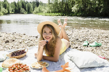 Frau mit Kirsche auf einer Decke am Flussufer liegend - VBUF00150
