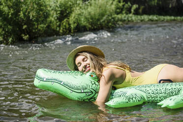 Woman embracing inflatable crocodile floating on river - VBUF00156