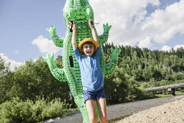 Fröhlicher Junge hält aufblasbares Krokodil an einem sonnigen Tag - VBUF00160