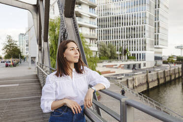 Smiling thoughtful woman leaning on railing on bridge - IHF01182