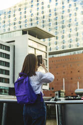 Woman with backpack photographing Elbphilharmonie through smart phone, Hafencity, Hamburg, Germany - IHF01192