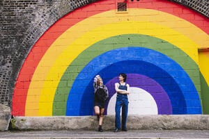 Freunde stehen zusammen vor einem an die Wand gemalten Regenbogen - AMWF00823