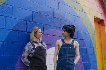 Young man and woman standing by rainbow painted on wall - AMWF00826