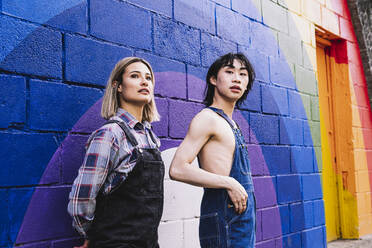 Young woman standing by man in front of rainbow painted on wall - AMWF00827