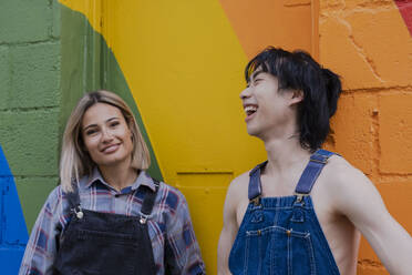 Junge Freunde hängen miteinander ab und stehen vor einem an die Wand gemalten Regenbogen - AMWF00832