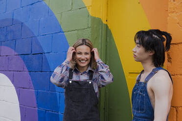Cheerful woman standing next to man in front of rainbow mural - AMWF00834