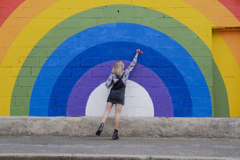 Junge Frau malt auf Regenbogen-Wandbild - AMWF00838