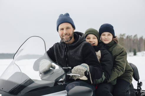 Ein Mann, der im Winter mit zwei Jungen auf einem Schneemobil unterwegs ist - MASF31448