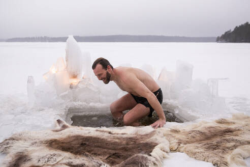 Fröhlicher reifer Mann genießt Eisbad auf zugefrorenem See im Urlaub - MASF31505