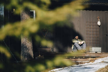 Älterer Mann sitzt auf der Veranda an einem sonnigen Tag im Winter - MASF31514