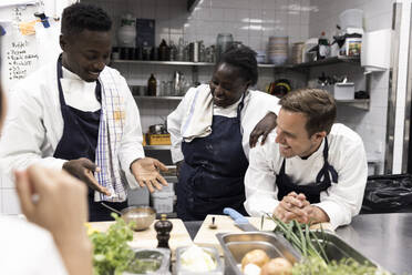 Chef explaining smiling multiracial colleagues at kitchen in restaurant - MASF31572