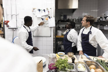 Männlicher Chefkoch erklärt seinen Kollegen am Whiteboard in der Küche eines Restaurants - MASF31575