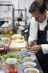 Koch garniert Suppe mit Basilikumblättern an der Küchentheke im Restaurant - MASF31596