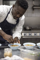 Männlicher Koch wischt Schüssel mit Suppe bei der Arbeit im Restaurant ab - MASF31599