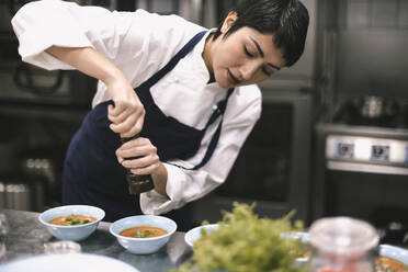 Female chef adding pepper in soup at kitchen counter in restaurant - MASF31608