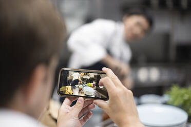 Koch fotografiert Kollegen bei der Zubereitung von Speisen im Restaurant - MASF31609