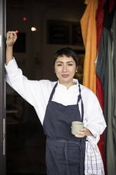 Porträt eines Restaurantbesitzers, der eine Tasse hält, während er am Eingang steht - MASF31628