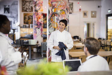 Lächelnde weibliche Köchin mit Schürze diskutiert mit multiethnischen Kollegen in einem Restaurant - MASF31636