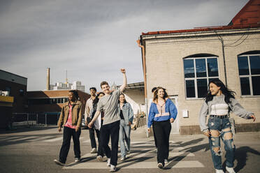 Happy multiracial young friends crossing street in city - MASF31650