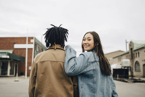 Smiling woman looking over shoulder while walking with friend on street - MASF31687