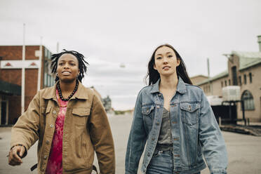 Confident young woman walking with friend on street in city - MASF31688