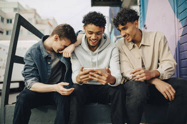 Happy man using smart phone while sitting with friends outdoors - MASF31698