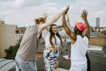 Glückliche multirassische Freunde und Freundinnen mit erhobenen Armen, die sich auf dem Dach gegenseitig abklatschen - MASF31719