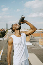 Young man drinking water from bottle on rooftop during sunny day - MASF31724