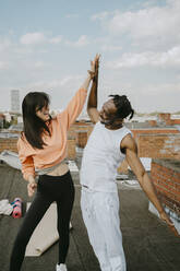 Cheerful woman giving high-five to male friend on rooftop - MASF31726