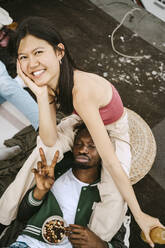 Porträt einer glücklichen jungen Frau mit einem männlichen Freund, der auf einer Dachterrassenparty das Friedenszeichen macht - MASF31765