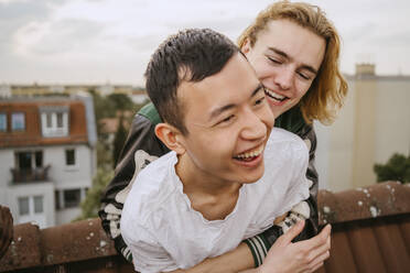 Cheerful young man embracing male friend while enjoying together on rooftop - MASF31782