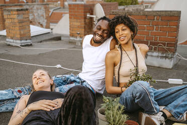 Junger Mann lacht, während er mit Freundinnen auf dem Dach sitzt - MASF31792