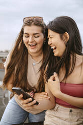 Young women laughing while sharing smart phone - MASF31795