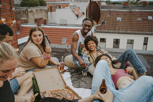Glückliche männliche und weibliche Freunde mit Pizza bei einer Party auf dem Dach - MASF31803
