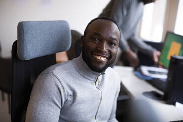 Portrait of smiling businessman sitting on chair in office - MASF31836