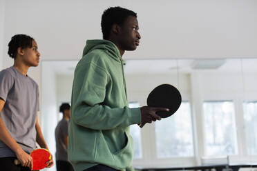 Man in green hoodie playing table tennis with friend in games room - MASF31850