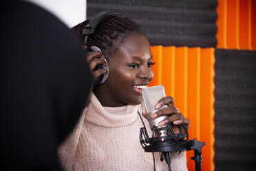 Smiling singer adjusting headphones while recording song in studio - MASF31919