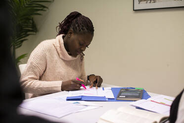 Portrait of female student using highlighter on paper while sitting in classroom - MASF31931