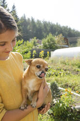 Smiling girl carrying dog in garden - LESF00104