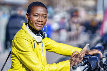 Young woman with smart phone at bicycle station on sunny day - GGGF01145