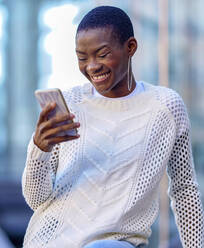 Frau mit Reif-Ohrring schaut auf ihr Smartphone und lächelt - GGGF01175