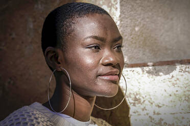 Woman wearing hoop earrings by wall on sunny day - GGGF01191