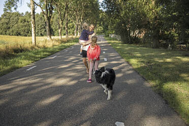 Mutter geht mit Töchtern und Hund auf der Straße spazieren - DWF00584