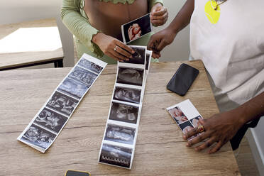 Pregnant woman by man with ultrasound photos of baby on table - GGGF01211