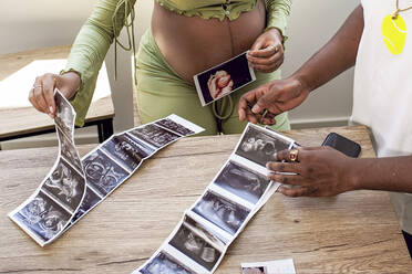 Pregnant woman arranging ultrasound photo of baby with man at home - GGGF01212